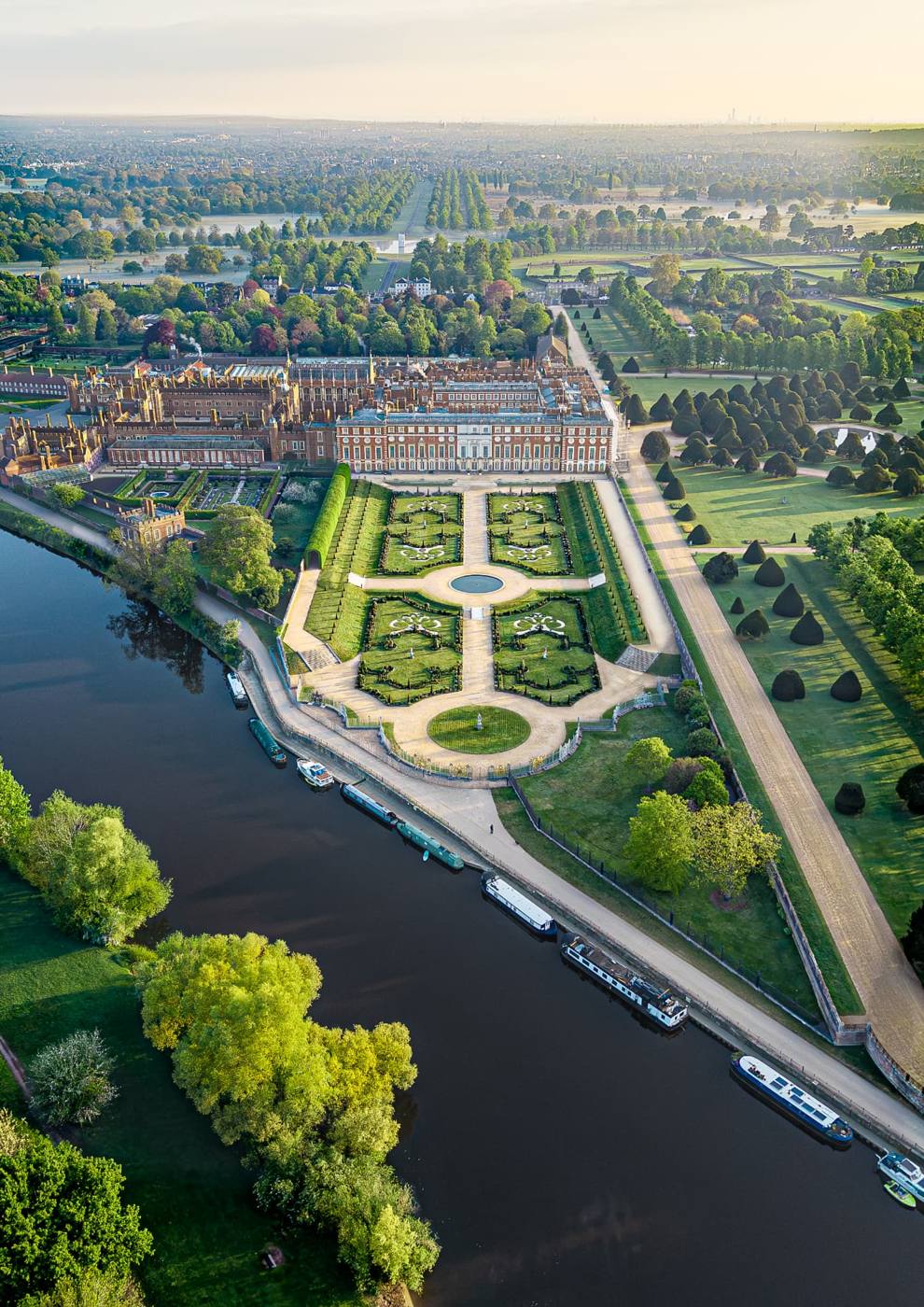 Aerial view of a riverside palace and formal gardens at sunrise